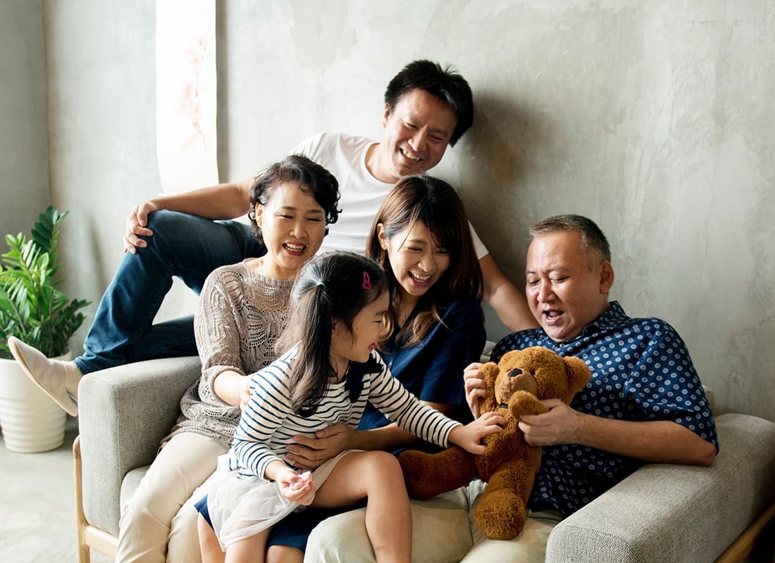 Insurance Solutions - View of Parents Grandparents and a Young Girl Having Fun Spending Time Together in the Living Room While Playing with a Teddy Bear