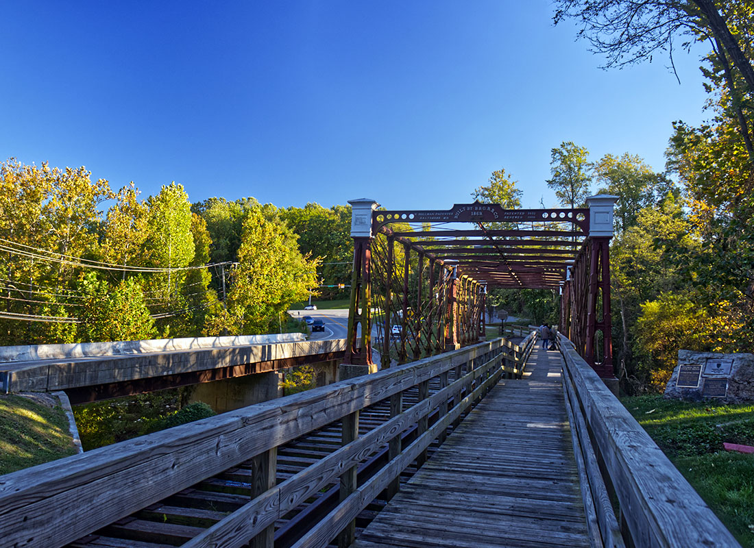 Laurel, MD - View of an Old Steel Wooden Bridge Surrounded by Green Foliage in Laurel Maryland Against a Bright Blue Sky