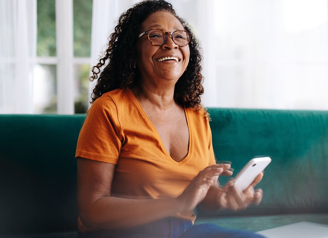 Service Center - Closeup Portrait of a Cheerful Senior Woman Sitting on a Sofa While Holding a Phone in her Hands