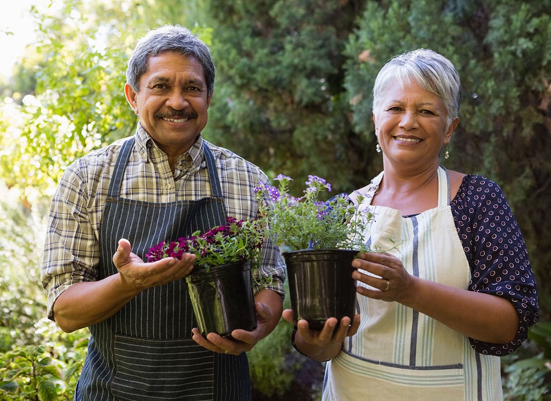 We Are Independent - Portrait of a Cheerful Senior Couple Standing Outside in the Backyard Holding a Pot of Flowers on a Sunny Day